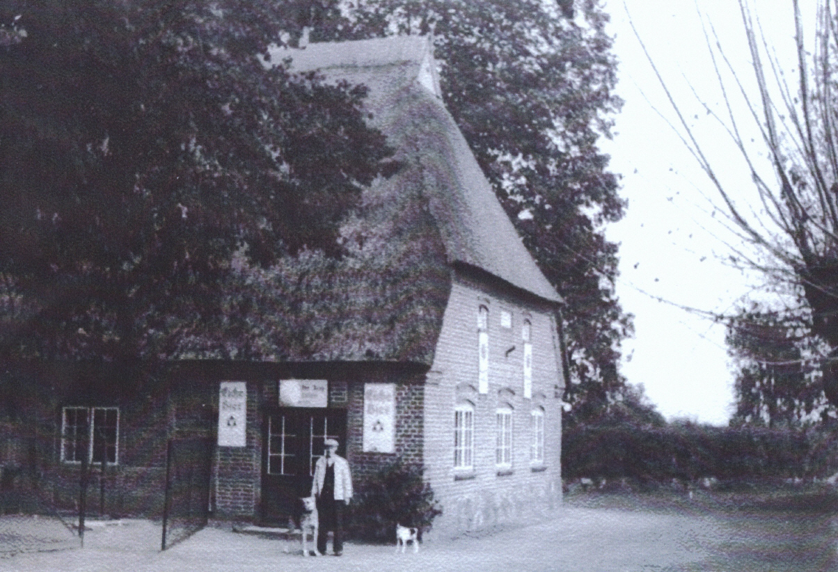 Ca. 1930: Der "Utspann" ist zugemauert, das Reetdach weist bereits erste Moos- und Verwitterungsspuren auf - aber:
Die Hoflinden sind mächtig und am neuen Eingang (dem ehemalien Utspann...) prangen links und rechts 2 weitere große Werbetafeln der Eiche-Brauerei.
Es scheint so, als sei hier seinerzeit ein erklecklicher Gewinn für die Brauerei - durch die Kehlen der Bauern und Knechte - in die Taschen des Brauereiherrn geflossen.