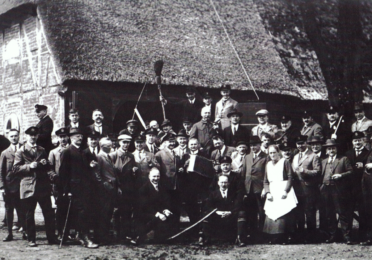 Dieses ist eines der frühesten, im Familienbesitz befindlichen Fotos vom Blickstedter Krug Otto Einfeldt sen. (Es muss ca. 1914 zur Pachtzeit entstanden sein. 1920 hat Horst sein Opa den gesamten Landbesitz samt Hofstelle gekauft. Er war Zahlmeister beim Bau des Kaiser-Wilhelm Kanals - heute Nord-Ostsee-Kanal)
Ganz deutlich ist zu erkennen, dass die Hauswände noch aus dem ursprünglichen Fachwerk bestehen, das Reetdach relativ unbeschädigt und ansehnlich ist.
Die Gruppe der feierlustigen und stattlichen Herren aus Dorf und Umgebung verdeckt fast ganz den rückseitigen "Utspann", den Unterstand für Kutschen und Pferde, der einmal quer durchs Haus ging. Eine Seite rein, andere Seite wieder raus..
Die Frau in der weißen Kittelschürze ist die Frau von Otto Einfeldt senj.